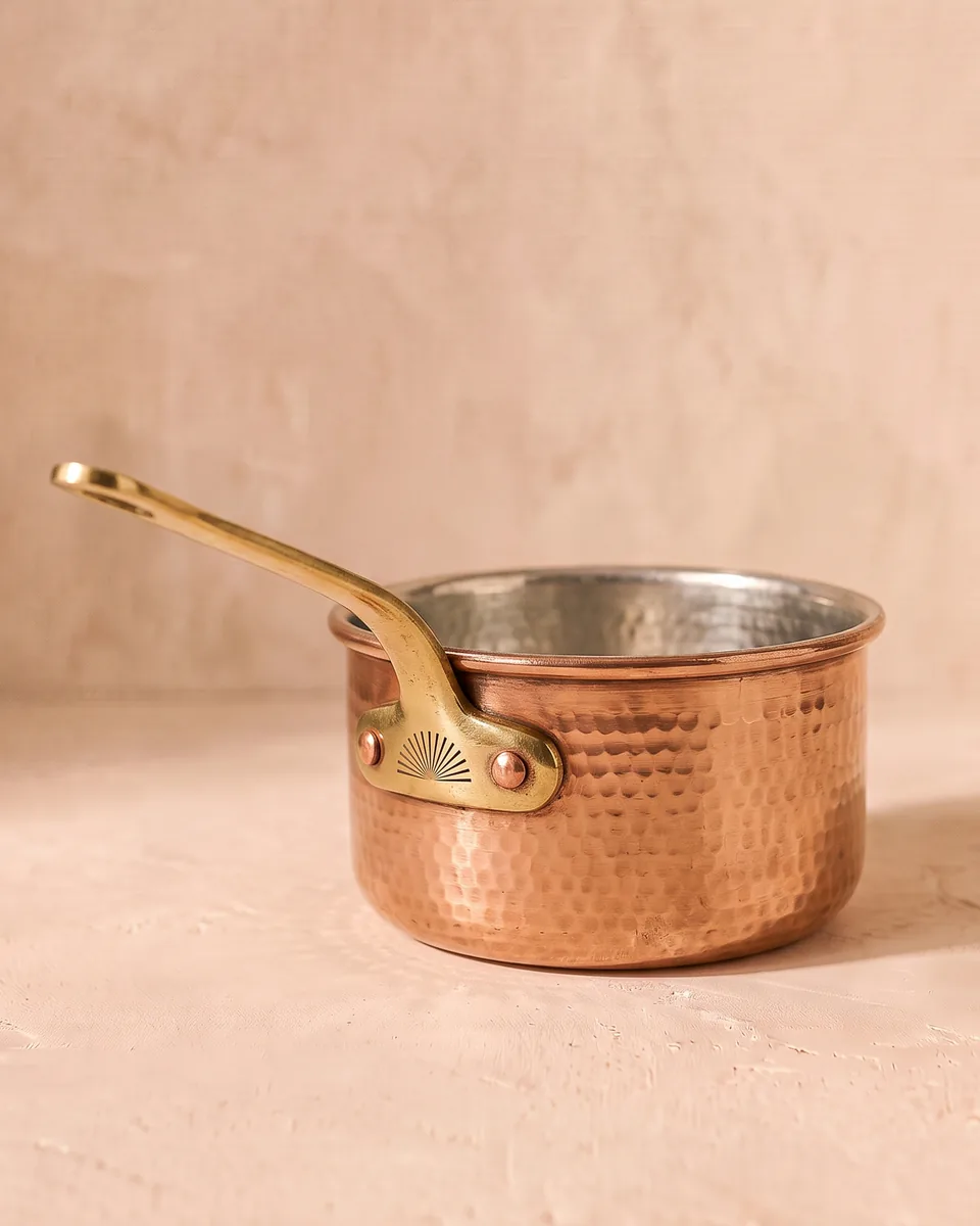 A hand-hammered copper chai pan with a brass handle.