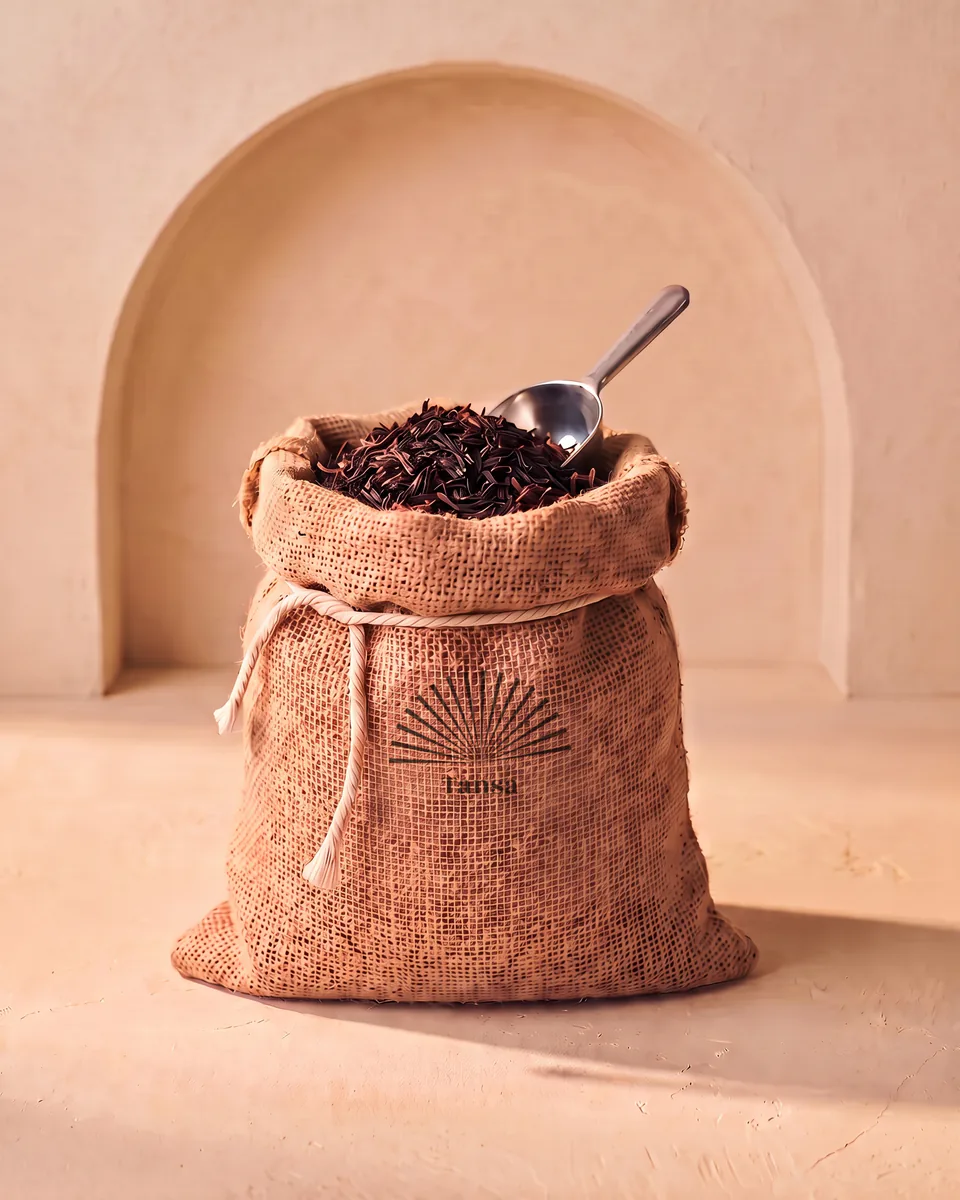 A hessian sack of loose tea stencilled with a sunburst, a steel scoop resting in it.
