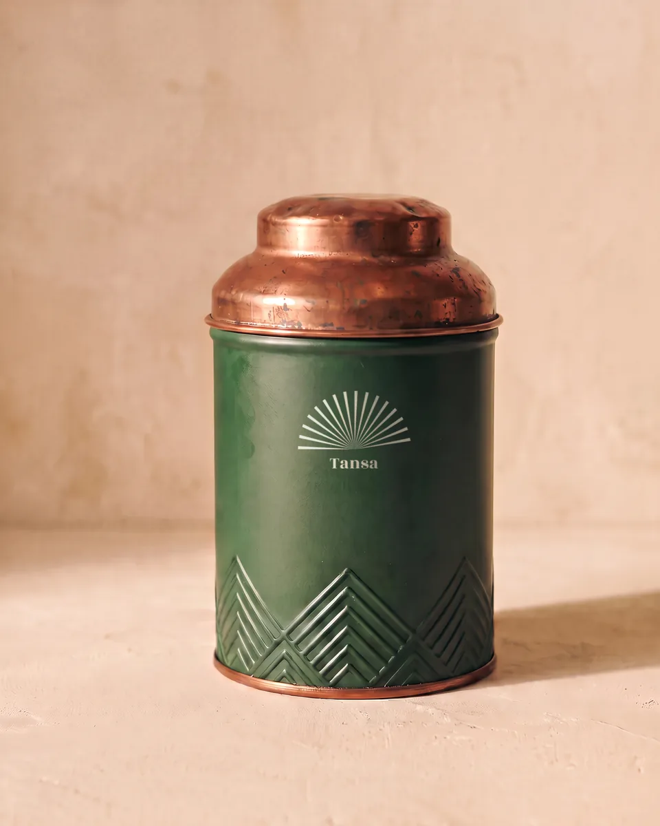 The house tin: bottle green with a copper lid and a cream sunburst.